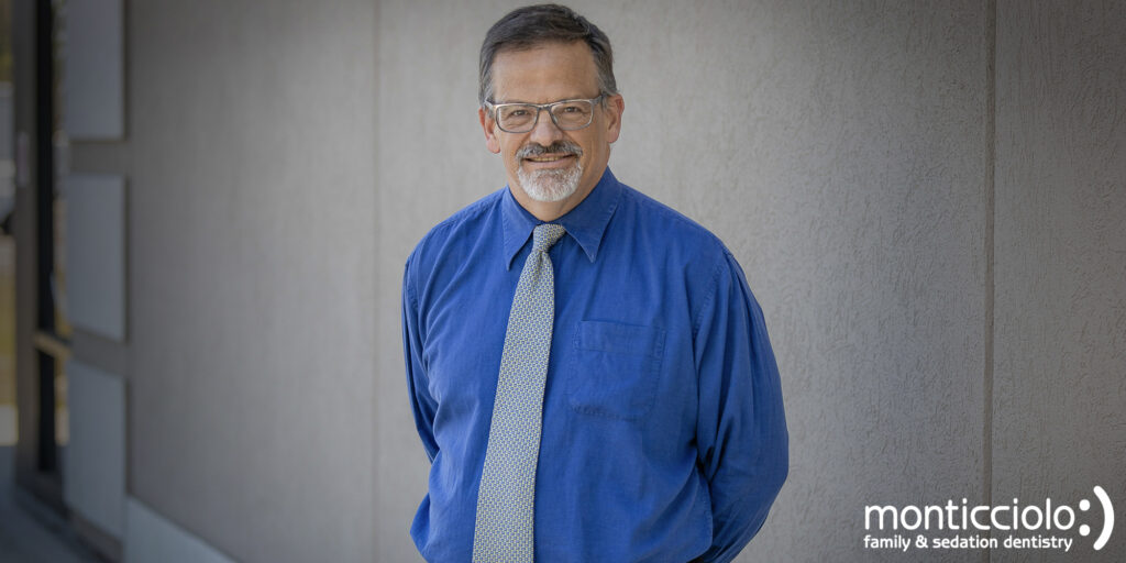 Smiling dentist in blue shirt and glasses.