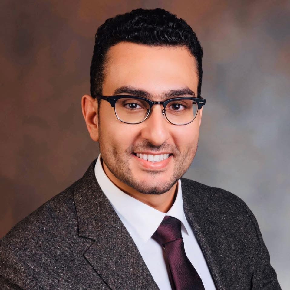 Man wearing glasses and a suit smiling.